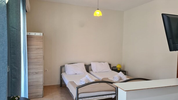 A room with a bed, bedside table, lamp, and a TV mounted on the wall. - Corfu Frodo Studios, Steps Away From the Beach (Corfu)