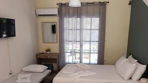Une chambre d’hôtel avec deux lits, une télévision, une fenêtre avec des rideaux, une petite table et une lampe.