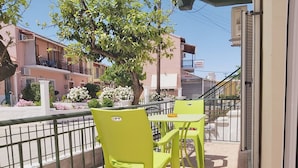A balcony with two green chairs and a table, a railing, and a view of a street with buildings and a tree. - Corfu Frodo Studios, Few Moments From the Beach (Corfu)