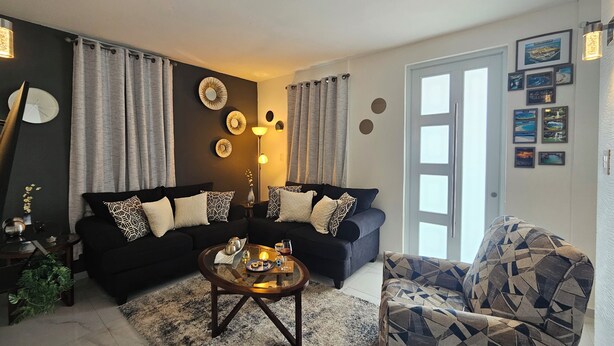 A living room with two black sofas, a patterned armchair, a coffee table, and a large window. - Villa De Gloria II - Elevated Signature Stay (Bayamon)