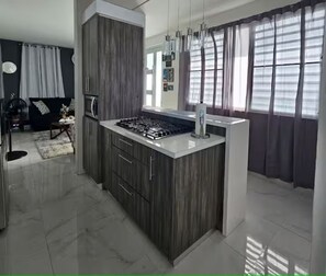 A modern kitchen with a central island, dark wood cabinets, and a white countertop. - Villa De Gloria II - Elevated Signature Stay (Bayamon)