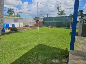 A grassy yard with a metal fence, a blue pole, and a small tree. - Villa De Gloria II - Elevated Signature Stay (Bayamon)