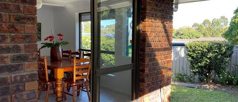 A patio with a table and chairs, a brick wall, and a sliding glass door leading to a garden.