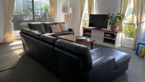 Een woonkamer met een zwarte leren bank, een houten salontafel, een televisie op een dressoir en een boekenkast.