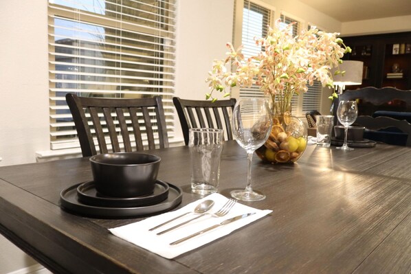 A dining table set with a bowl, cutlery, a vase with flowers, and wine glasses.