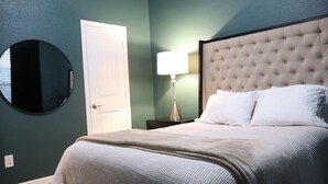 A bedroom with a tufted headboard, a round mirror, a bedside lamp, and a white door. - 4-bedroom house in adorable Midland  (Midland)