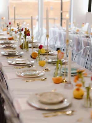 Une longue table dressée pour un événement formel, avec de la vaisselle en verre transparente, des assiettes et des bougies.