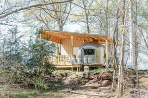 A mobile home with a wooden deck and a covered porch, surrounded by trees.