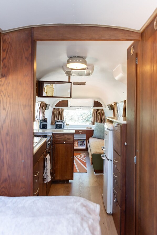 A compact RV interior with a kitchenette, a small seating area, and a bed.