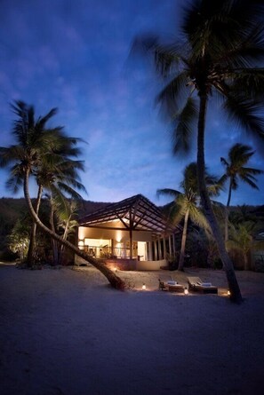 A beach house with a covered patio, palm trees, and lounge chairs. - Tadrai Island Resort Fiji (Mana Island)