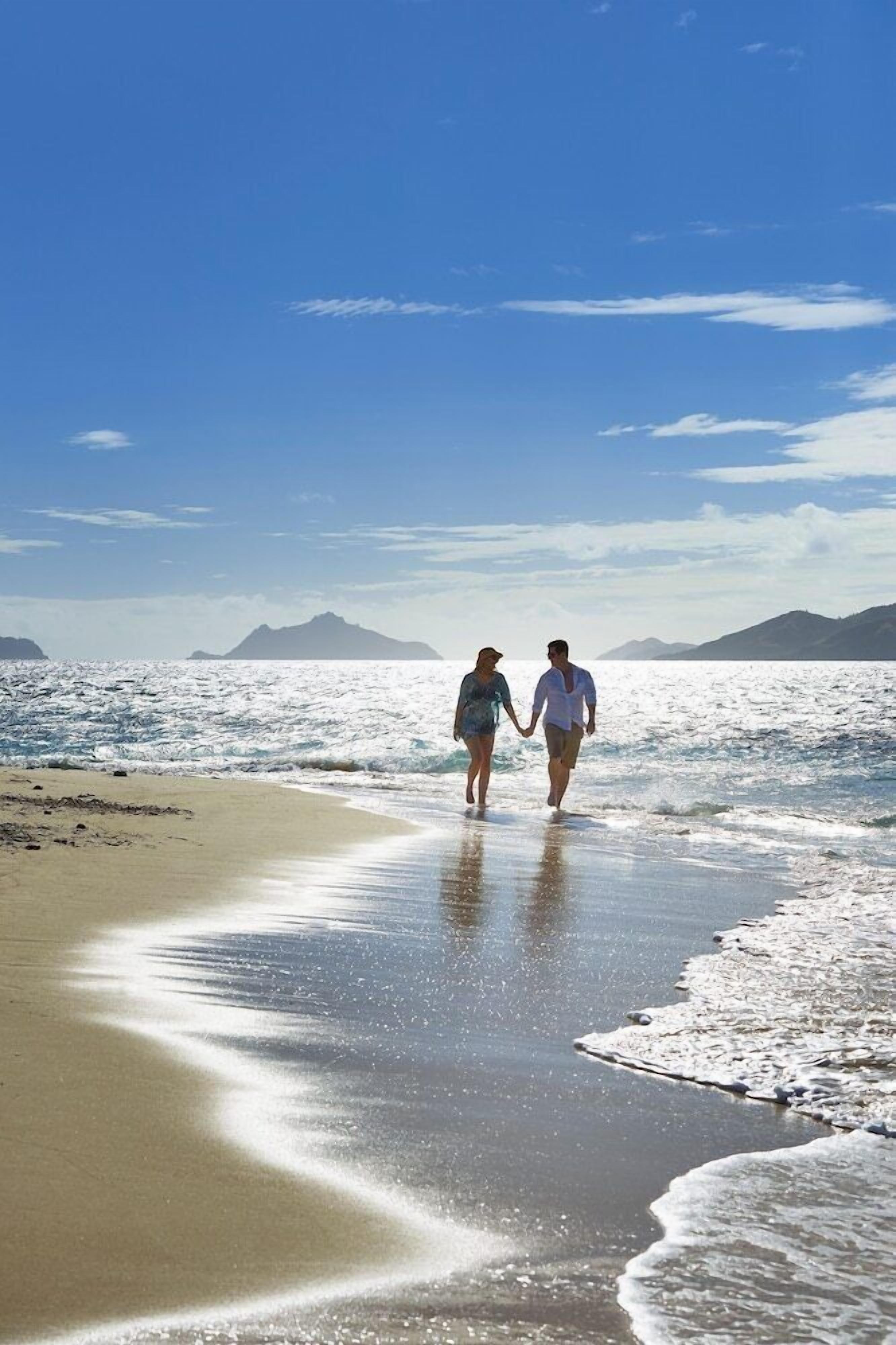 A beach with two people walking on the shore, a clear sky, and distant mountains.