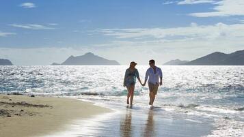 A beach with two people walking on the shore, a clear sky, and distant mountains.