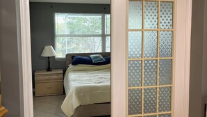 Un dormitorio con cama, mesita de noche, lámpara y ventana con persianas.