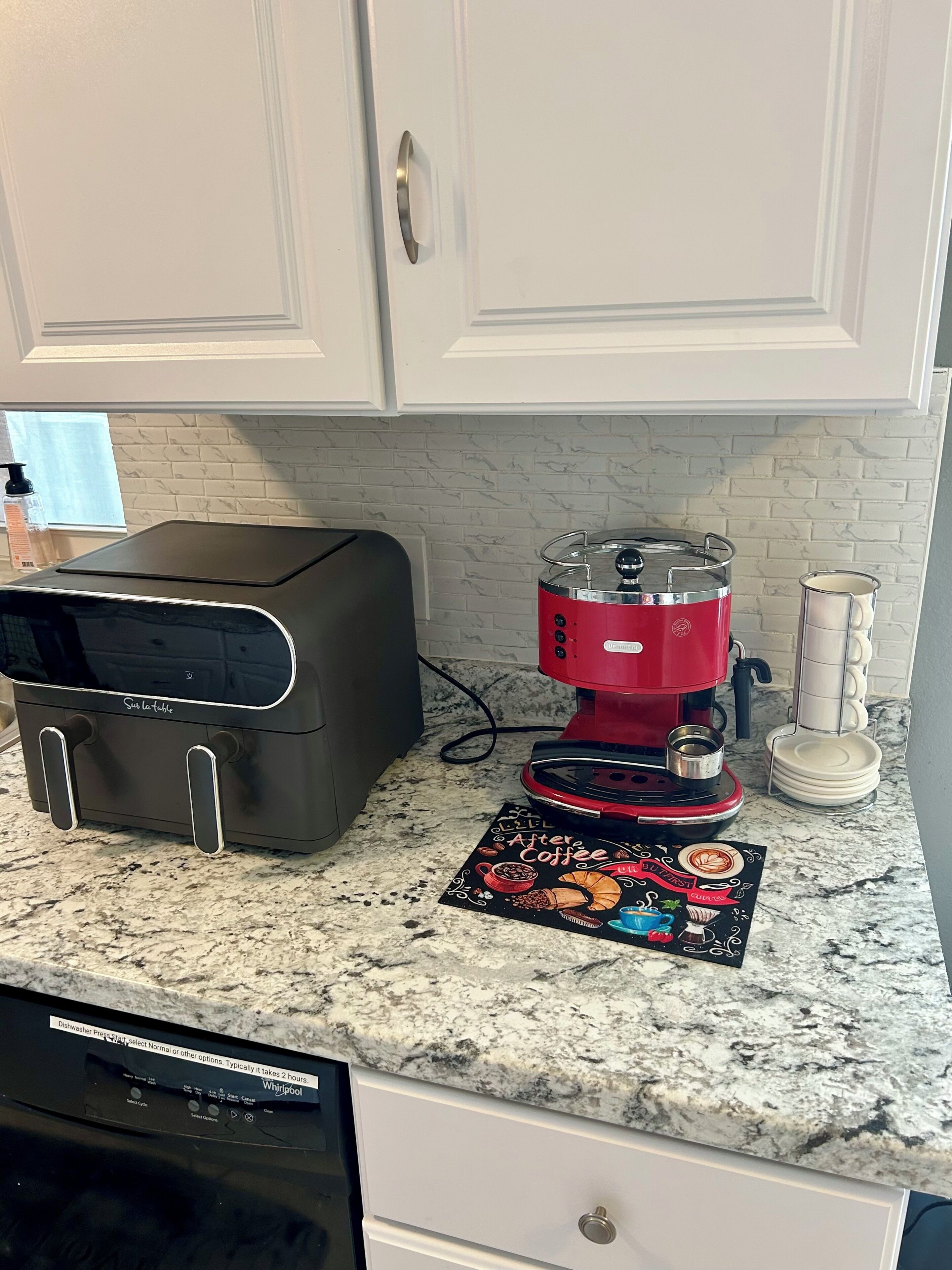 A kitchen with a toaster, a red coffee maker, a dish rack, and a coffee-themed placemat.