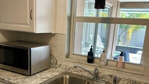 Una cocina con armarios blancos, un lavamanos doble de acero inoxidable, un microondas y una ventana con vistas al exterior.