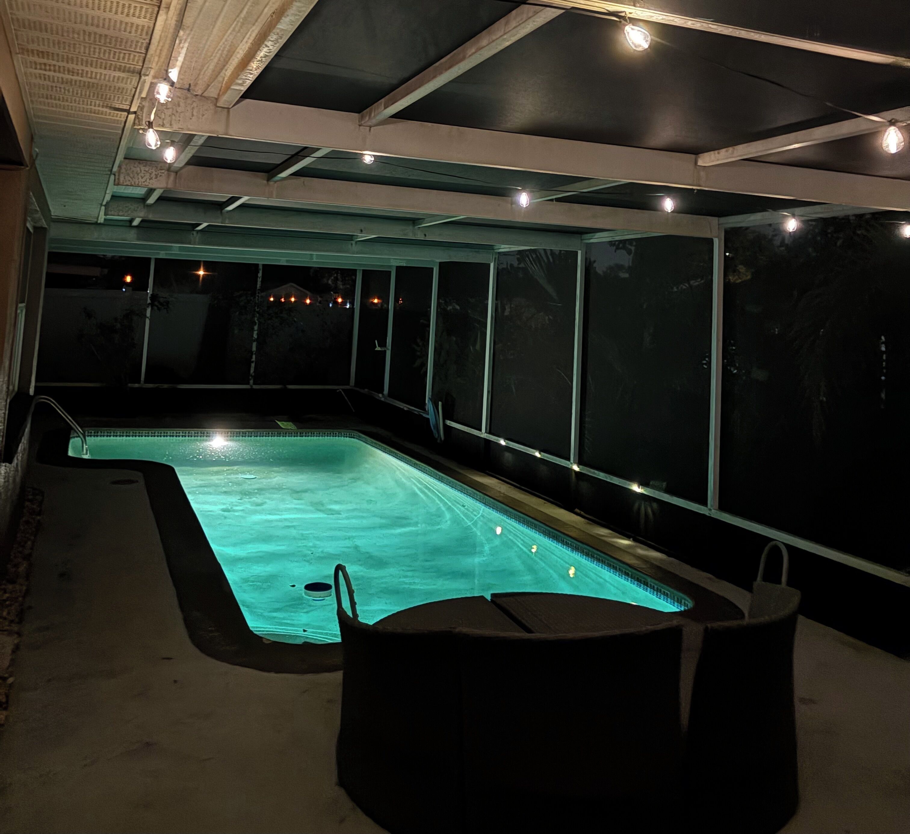 An indoor swimming pool with a clear view of the ceiling and walls, a poolside seating area, and a view of the outside at night.