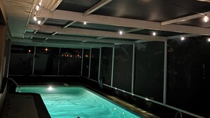 Una piscina interior con vistas claras al techo y a las paredes, un área de descanso junto a la piscina y vista al exterior de noche.