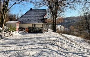 A snow-covered landscape with a house, a fenced yard, and a hill in the background.