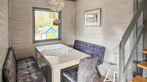 A room with a table and bench seating, a window with a view of a blue house, and a framed picture on the wall.