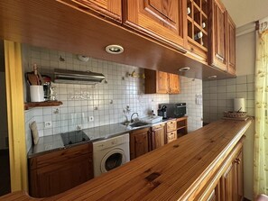 A kitchen with wooden cabinets, a washing machine, and a microwave. - Résidence Terrasses de l'Océan Apartment terrace and pking near beach (CAPBRETON)