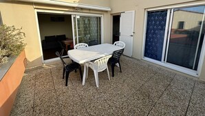 A patio with a table and chairs, a sliding glass door, and a small garden area. - Résidence Terrasses de l'Océan Apartment terrace and pking near beach (CAPBRETON)