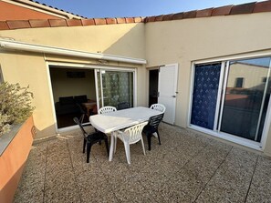 A patio with a table and chairs, a sliding glass door, and a small garden area. - Résidence Terrasses de l'Océan Apartment terrace and pking near beach (CAPBRETON)