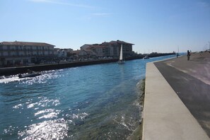 A waterfront promenade with buildings, a sailboat, and a cyclist. - Résidence Terrasses de l'Océan Apartment terrace and pking near beach (CAPBRETON)