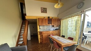 A dining area with a wooden table and chairs, a kitchen with wooden cabinets, a staircase, and a view through a glass door. - Résidence Terrasses de l'Océan Apartment terrace and pking near beach (CAPBRETON)