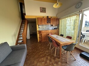 A dining area with a wooden table and chairs, a kitchen with wooden cabinets, a staircase, and a view through a glass door. - Résidence Terrasses de l'Océan Apartment terrace and pking near beach (CAPBRETON)