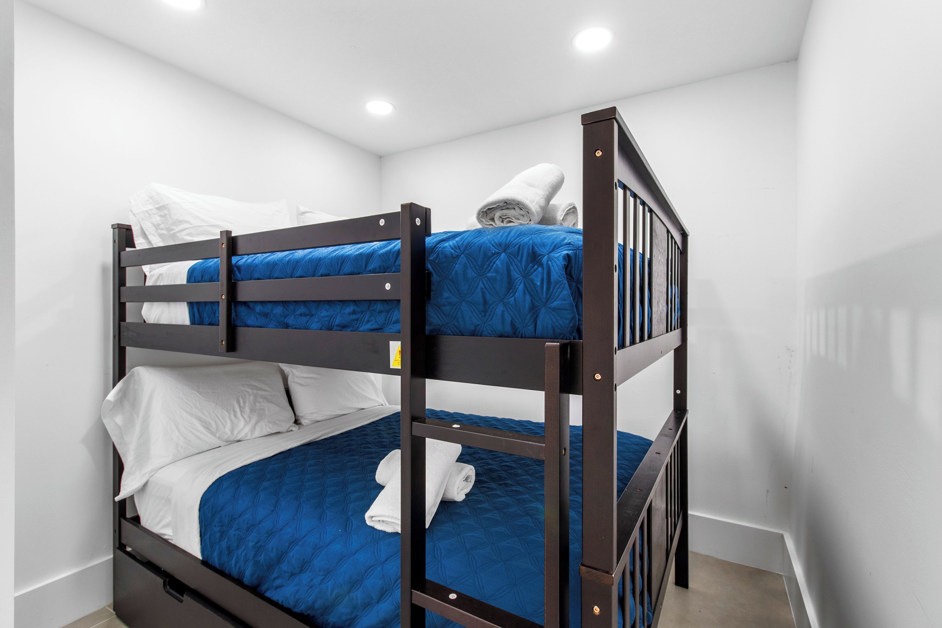 A bunk bed with blue bedding and white pillows, a wooden frame, and a small towel on the lower bunk.