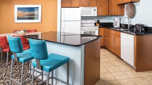 A compact kitchen with a central island, wooden cabinets, and a dining area with blue chairs.