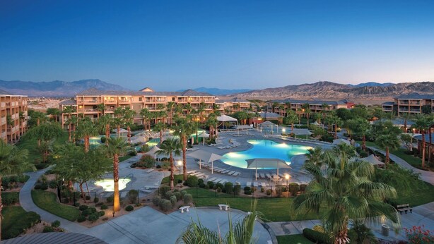 A resort with multiple buildings, a central pool area, and palm trees.