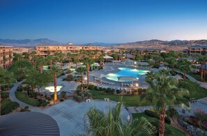 Un resort con varias edificaciones, un área de piscina central y palmeras.