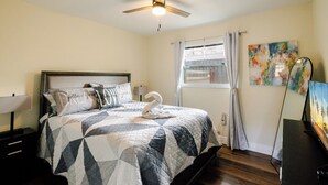 Ein Schlafzimmer mit Bett, Deckenventilator, Fenster mit Vorh ängen und einem Gemälde an der Wand.