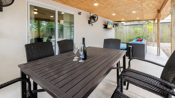 Ein überdachter Patio-Bereich mit Tisch, Stühlen und einer Weinflasche.