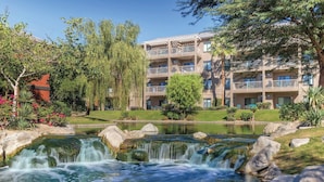 Un hotel con jardín ajardinado, un estanque con cascada y varios balcones.