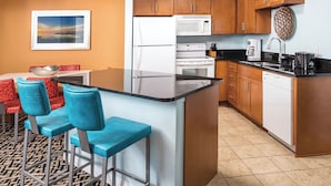 Cocina compacta con una isla central, armarios de madera y un comedor con sillas azules.