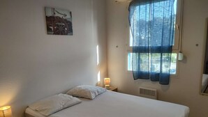 Ett sovrum med en säng, ett nattduksbord med en lampa, ett fönster med gardiner och en tavla som hänger på väggen.