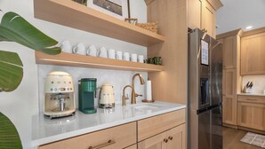 Une cuisine moderne dotée d’un réfrigérateur en acier inoxydable, de meubles en bois, d’un plan de travail blanc et d’une machine à café.