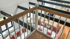 Un intérieur à plusieurs niveaux, avec un garde-corps d’escalier en bois, un coin repas comprenant une table et des chaises, et une vue sur un niveau inférieur où se trouve un canapé.