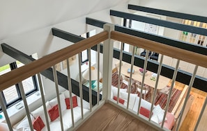 A multi-level interior with a wooden staircase railing, a dining area with a table and chairs, and a view of a lower level with a sofa.