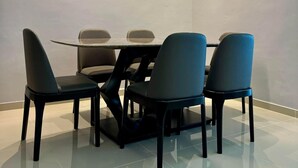 A modern dining area with a round table and four chairs, recessed ceiling lighting, and a plain wall.