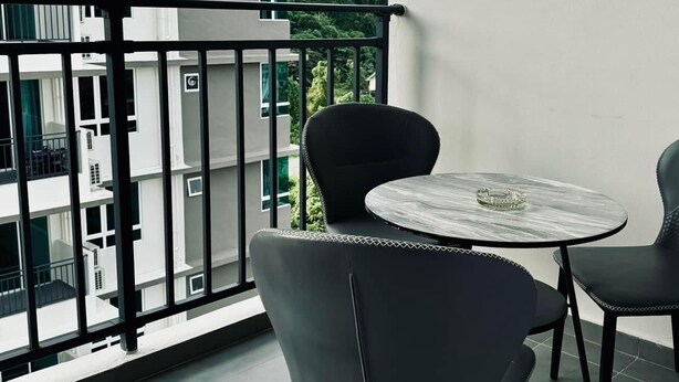 A balcony with a round table and two chairs, a view of a multi-story building, and a tiled floor.