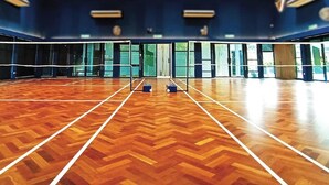An indoor sports hall with a wooden floor, a volleyball net, and large windows.