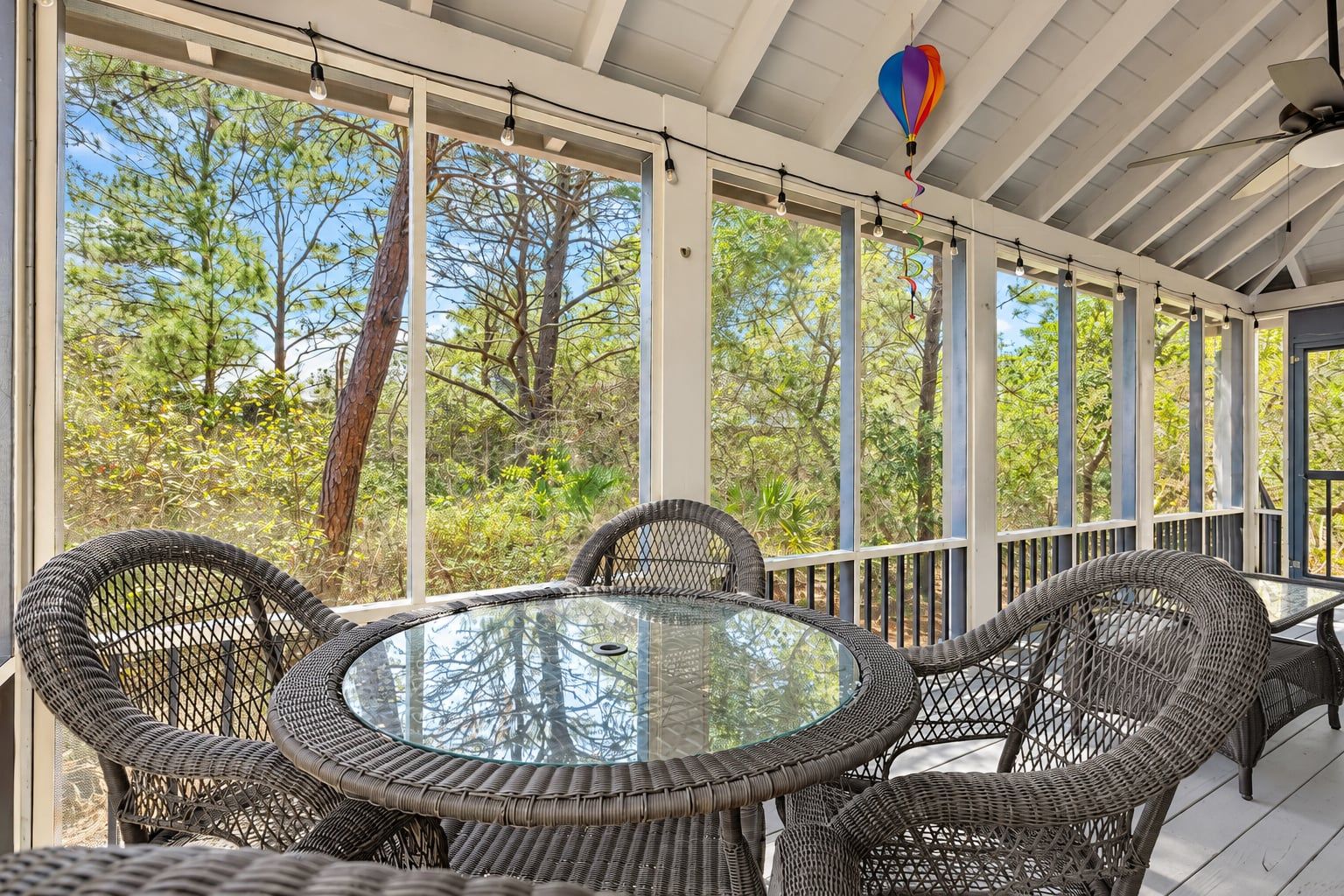 A covered outdoor seating area with wicker furniture and large windows offering a view of trees.