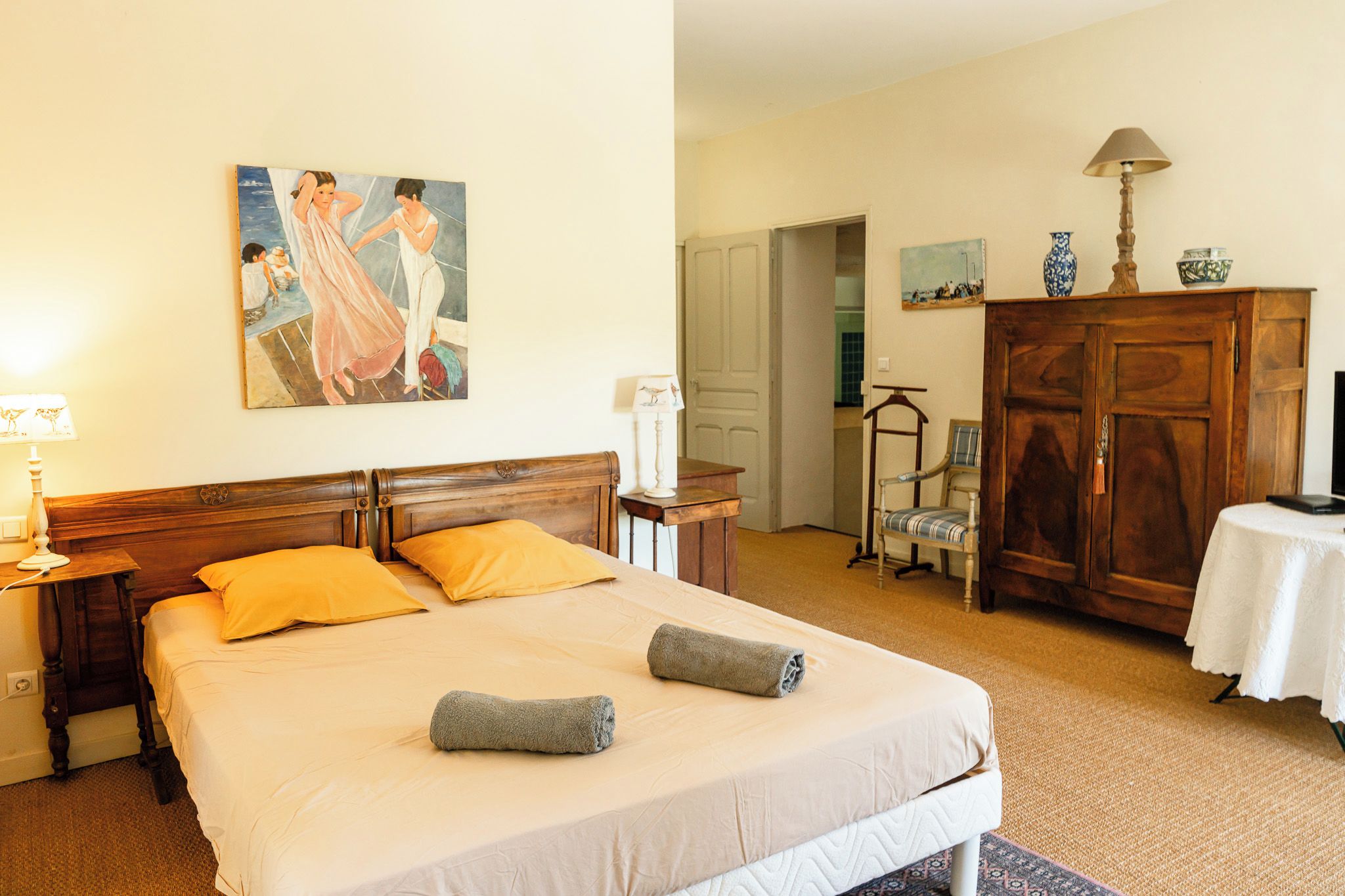 Una camera d'albergo con un letto, due lampade ai comodini, un quadro appeso al muro, un armadio in legno, una sedia e un tavolo con una lampada.