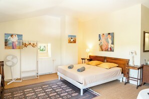 Un dormitorio con una cama, un radiador, una ventana, un ventilador y cuadros en las paredes.