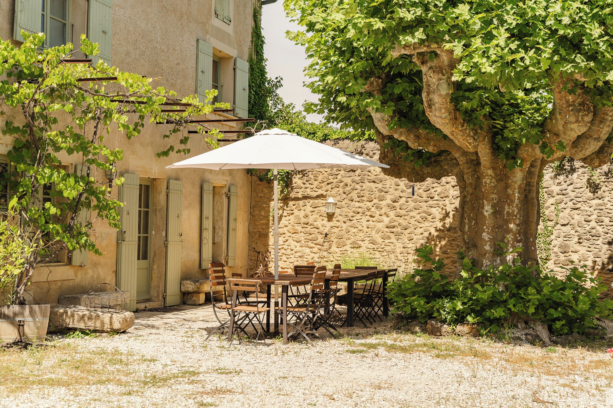 Un espace extérieur aménagé avec une table et des chaises, un parasol blanc et un mur en pierre.