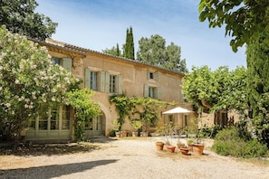 A rustic building with a courtyard, potted plants, and a table with chairs. - Maison Margerie - Provencal farmhouse with swimming pool and view of Mont Ventoux (Colonzelle)