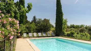 Une piscine rectangulaire à l’eau d’un bleu limpide, entourée d’une terrasse en béton. Cinq chaises longues sont alignées le long du bord de la piscine.